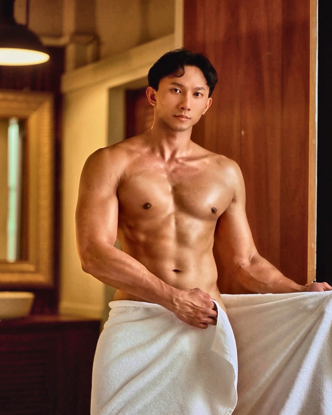 spicy somtam holding a white towel open at a hotel bathroom door, looking into the camera